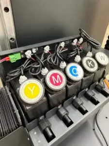 Close-up of the CMYK plus white UV ink reservoirs on the WP-UV-PRO wall printer — Yellow, Magenta, Cyan, Black, and White proprietary ink with labeled caps