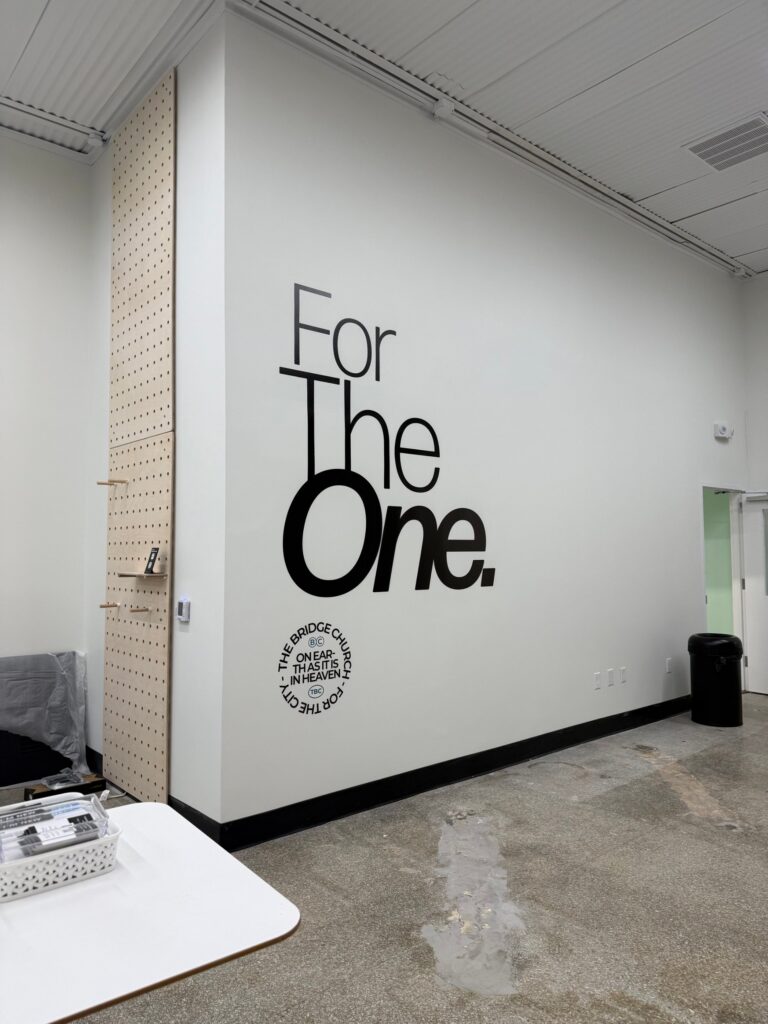 Finished For The One brand wall with The Bridge Church seal printed directly on a white wall