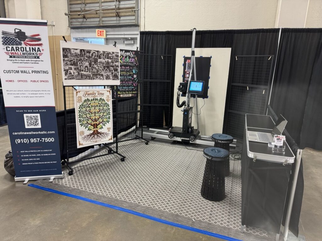 A trade show booth with a vertical printer on its track, printed sample boards and a Carolina Wallworks banner