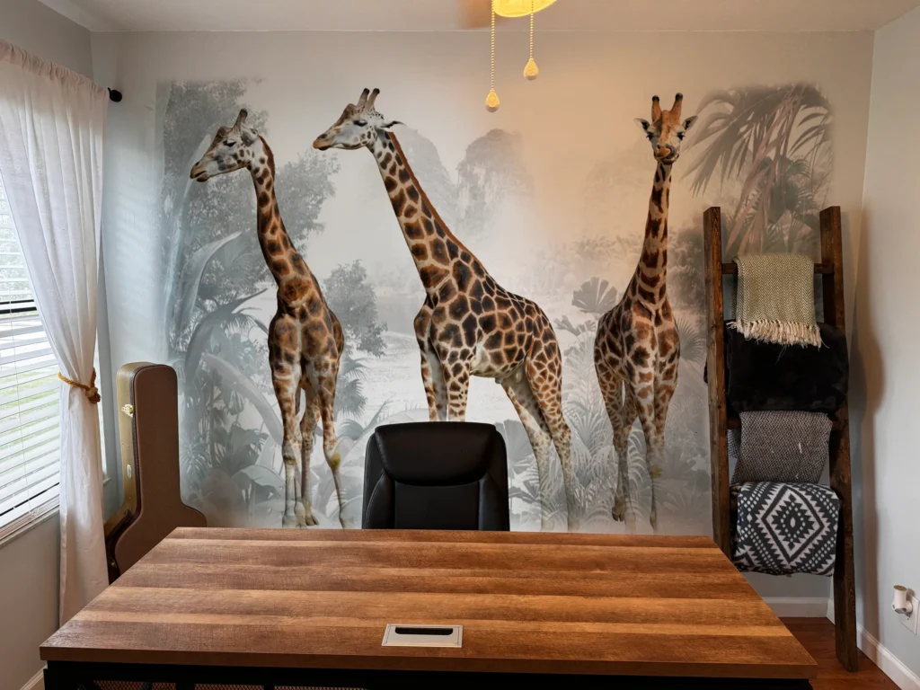 Three giraffes in a misty forest printed on a home office wall behind a desk