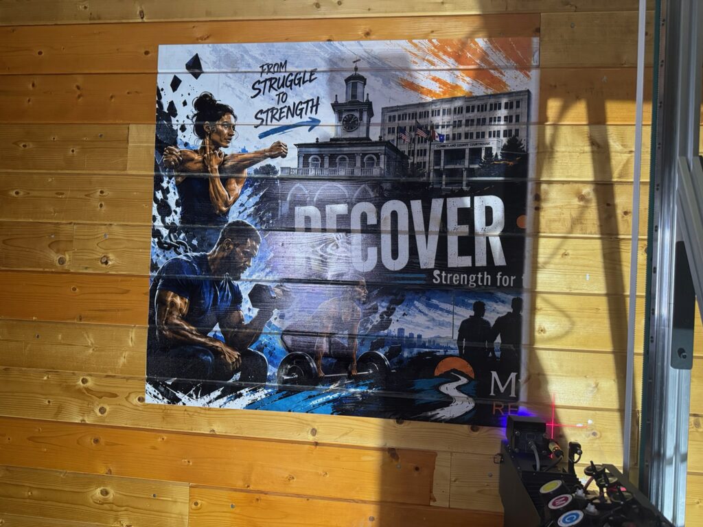 A fitness mural designed with AI, printed across a wall of wood slats, with the vertical printer and its laser guide at the right