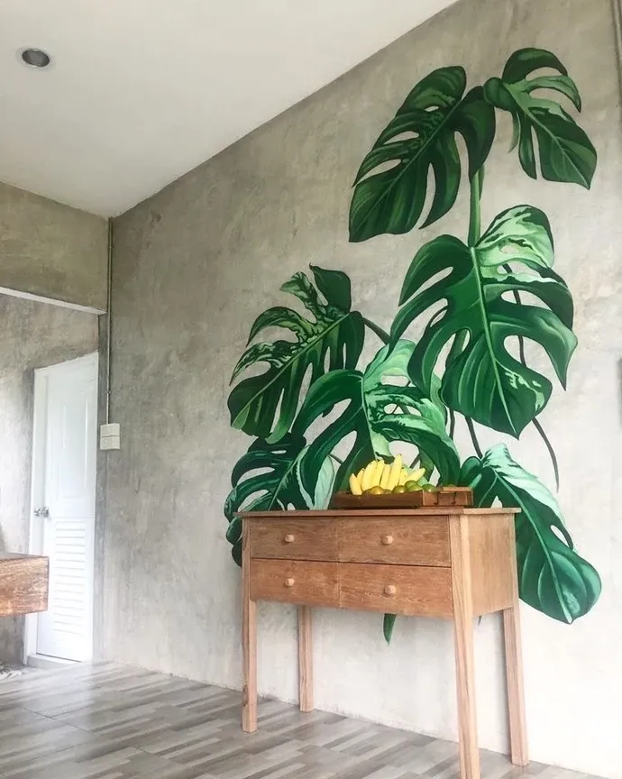 Large monstera leaves printed on a gray concrete wall above a wood console