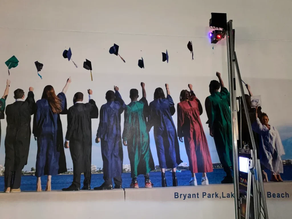Close-up of graduates tossing caps, printed on an exterior wall, with the printer rail at the right