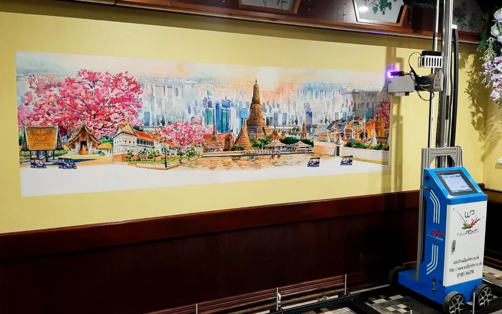 A cherry blossom city skyline printed across a yellow restaurant wall, with the vertical printer beside it
