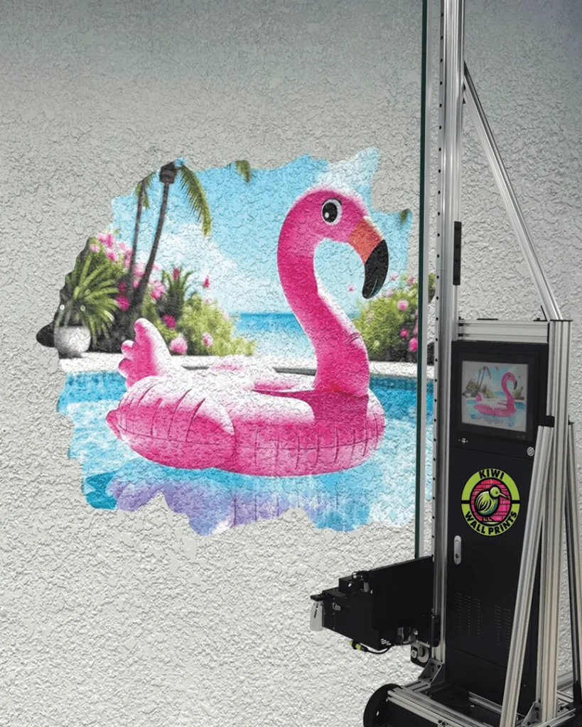 A pink flamingo pool float printed on a textured stucco wall, with the vertical printer beside it