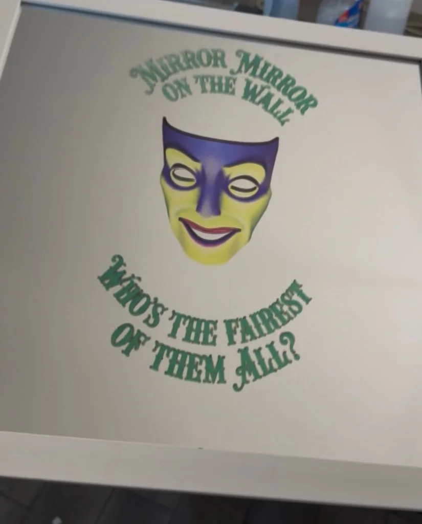 A theater mask and the words Mirror mirror on the wall printed on a white surface