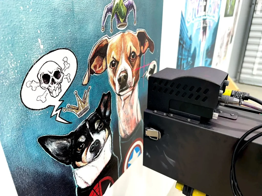 Two dog portraits printed on a blue wall, with the print carriage in the foreground