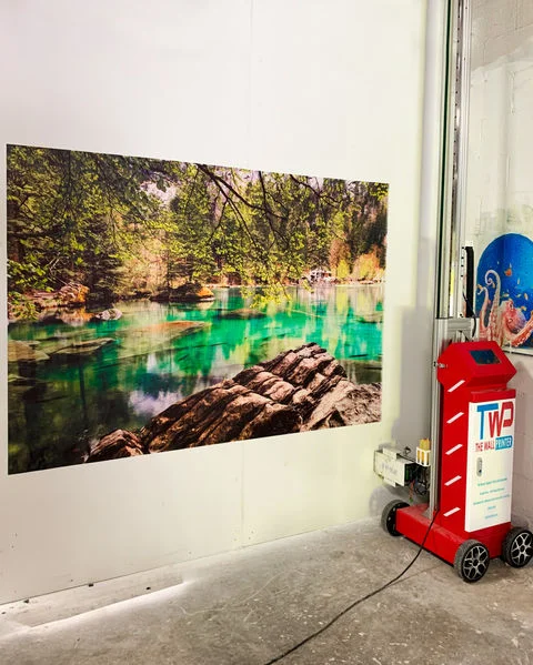 A forest river scene printed on a white wall, with the printer's base at the right