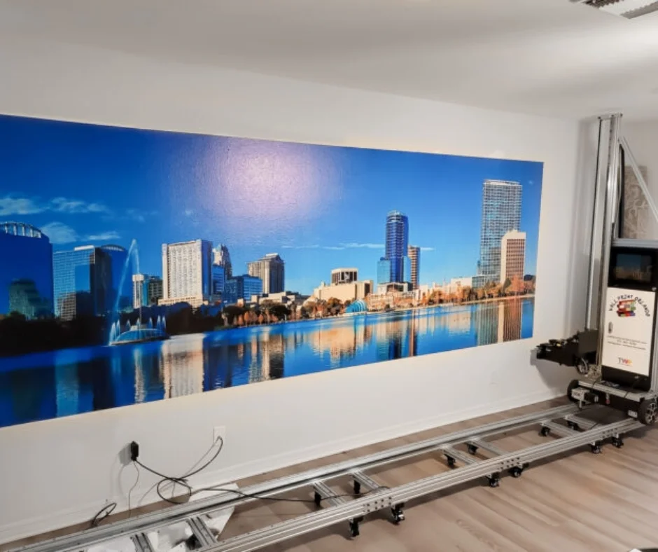 A city skyline over the water printed across a long wall, with the vertical printer on its track