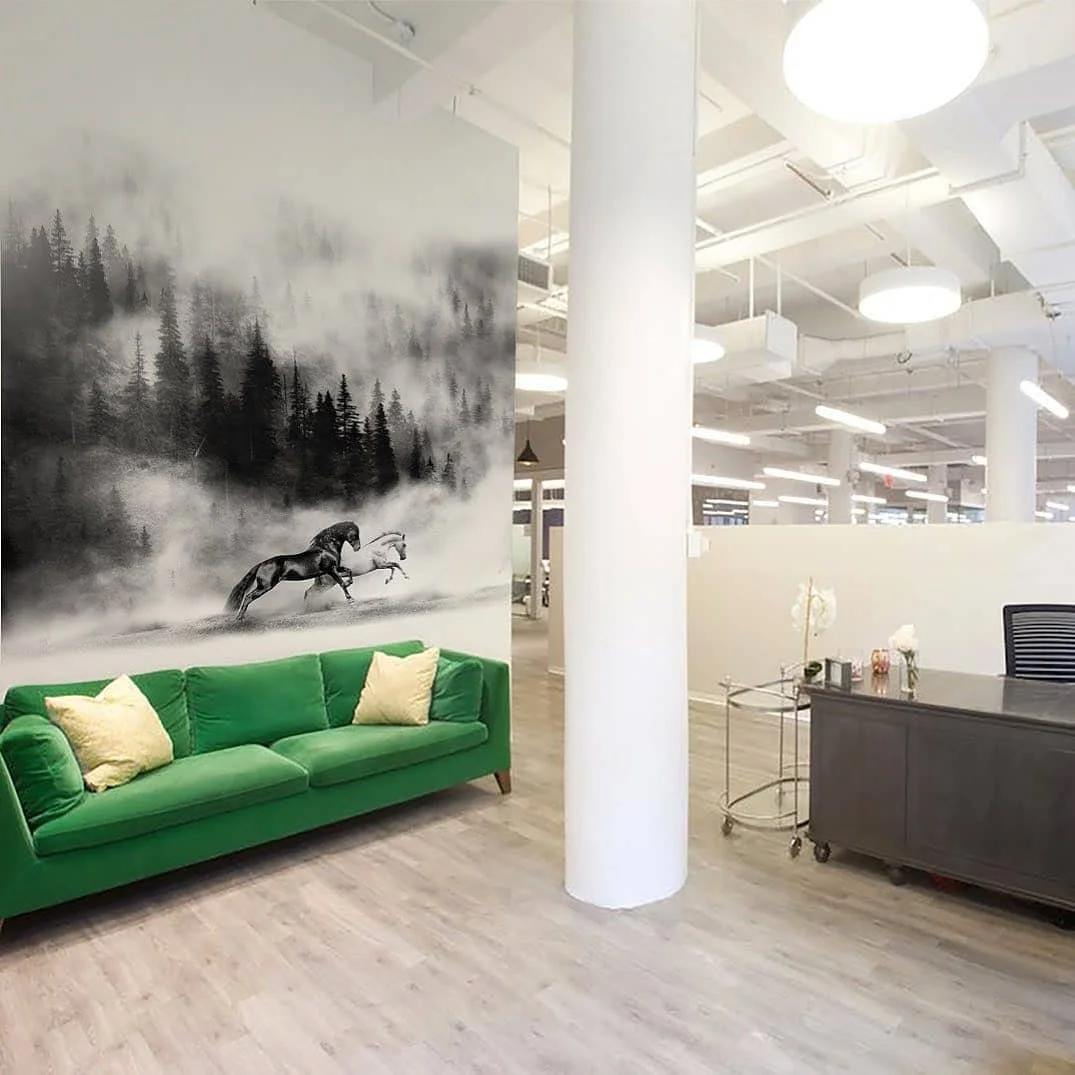 Horses running through a misty forest, printed on an office wall above a green sofa