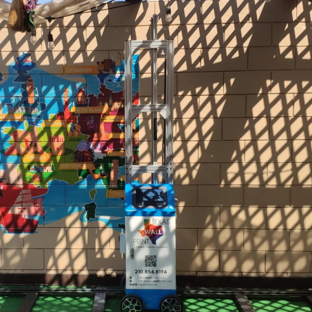 A colorful map printed on an outdoor block wall, with the printer on its track in front