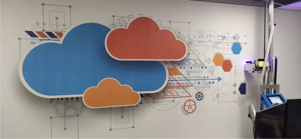 Colored cloud shapes and a technical line drawing printed on an office wall, with the printer at the right