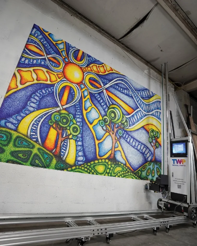A vertical printer on its track beside a sun mural printed on a painted block wall