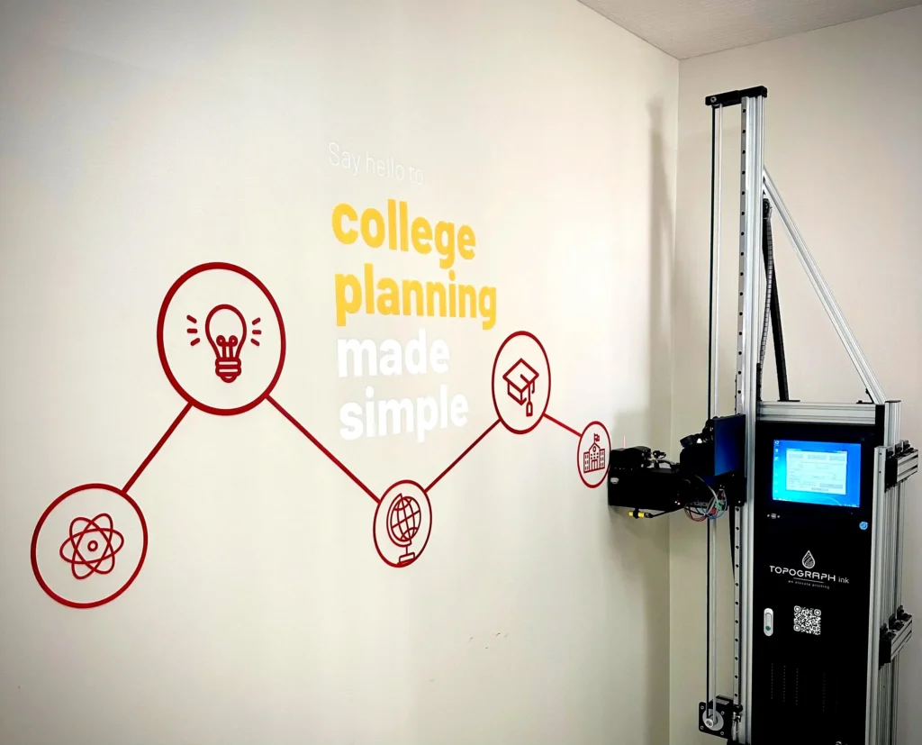A college planning logo and icons being printed on an office wall, with the vertical printer beside it