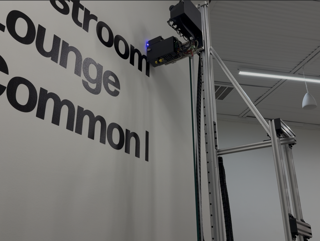 Close-up of a UV wall printer printhead printing black wayfinding lettering on a painted wall