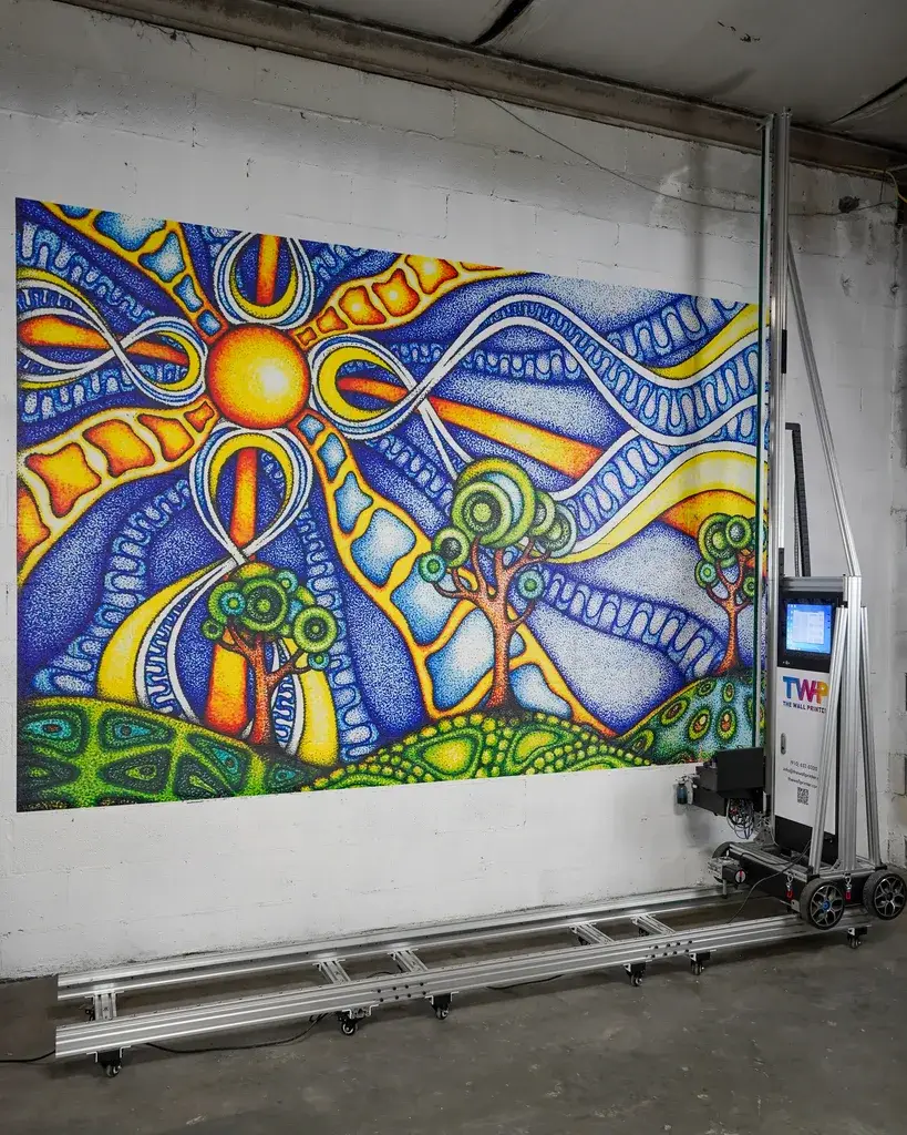 The Wall Printer on its floor track beside a full-color sun and trees mural printed on a white cinder block wall
