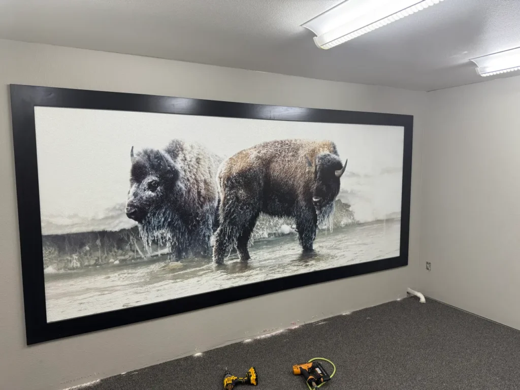 Two bison in a snowy river printed on an office wall inside a black frame, by Wy Not Print