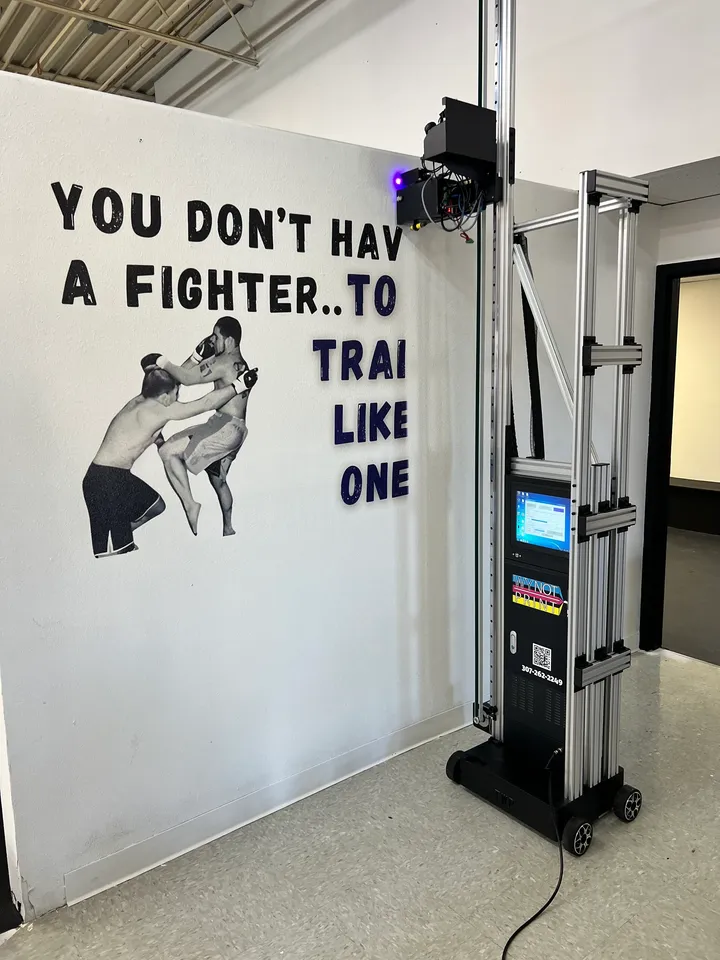 A gym wall graphic mid-print, with the Wy Not Print printer at the wall